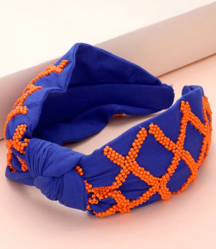 Royal blue knot headband with orange beaded crisscross pattern. Available in one size.