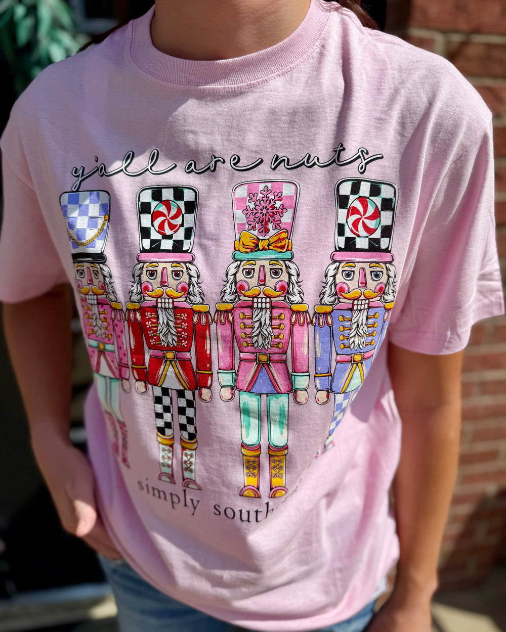 Pink Simply Southern “Y’all Are Nuts” tee with four colorful nutcrackers and festive text; available in sizes S-XXL.