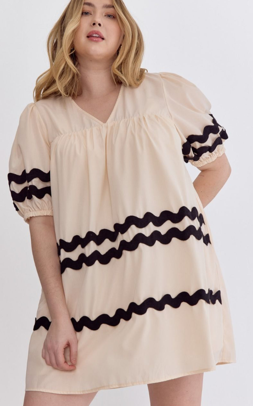 The Bay Ribbon Dress offers a chic cream color embellished with black wavy lines on the sleeves and midsection. The dress features puffed sleeves and a loose fit. Available sizes include Small, Medium, Large, and Extra-Large.