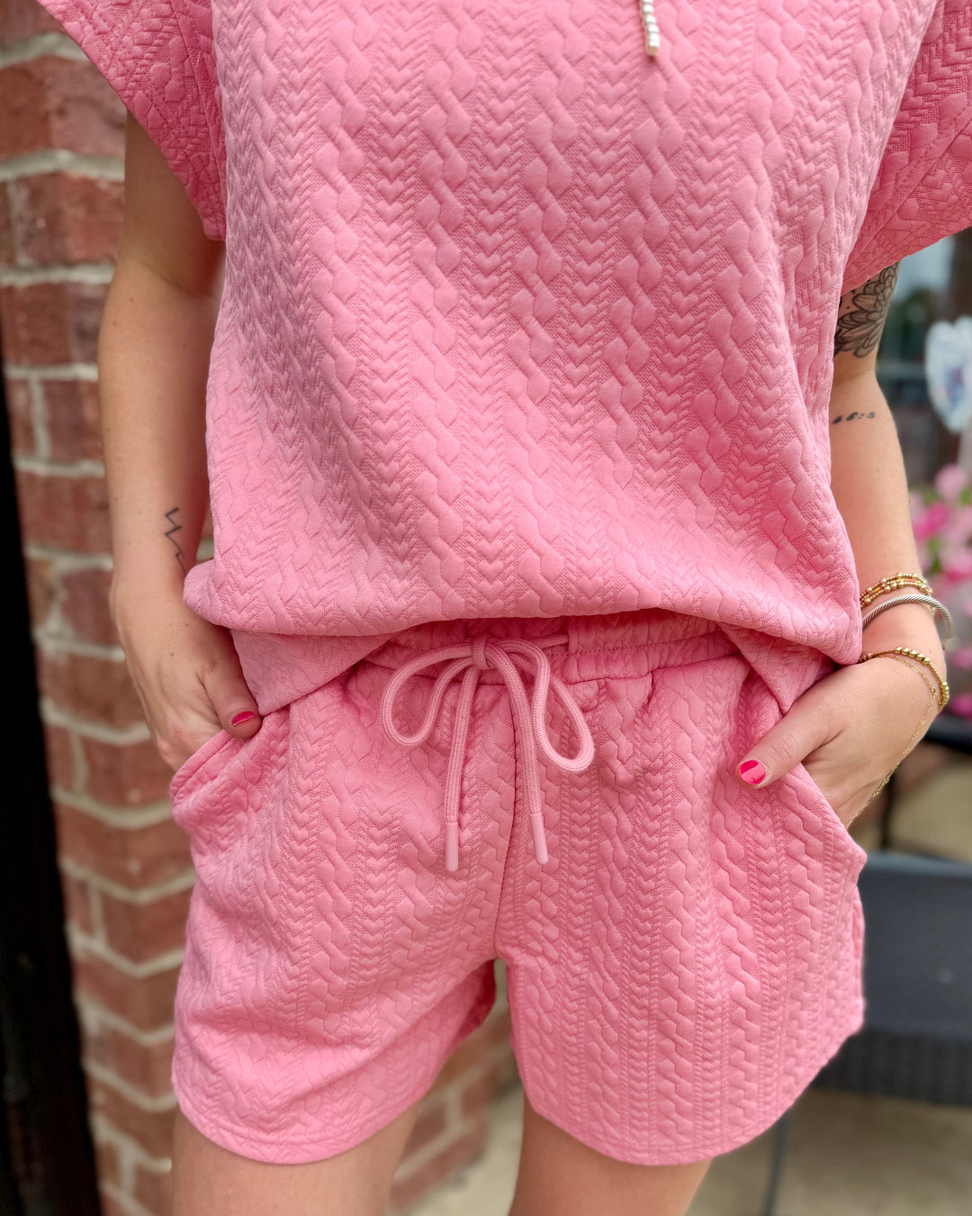 The Pearl Pink Ribbon Trim Textured Set includes a bubblegum pink short-sleeve top and matching drawstring shorts; available in sizes XS to XL.