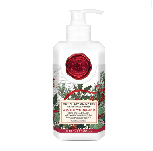 Winter Woodland Hand & Body Lotion by Michel Design Works. 12 fl oz (354 ml). Enriched with shea butter and botanical ingredients. Features a white bottle with red flowers, green foliage, and a red seal design. Perfect for winter.