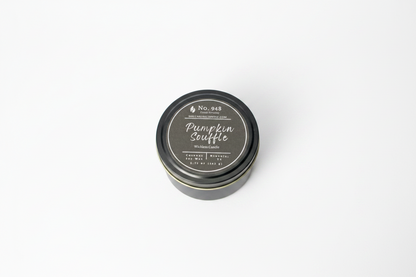 A small, round black tin labeled "Wickless Candle 5.75 oz" in coconut soy wax with "Pumpkin Souffle" and product details on the lid; available in 5.75 oz size.