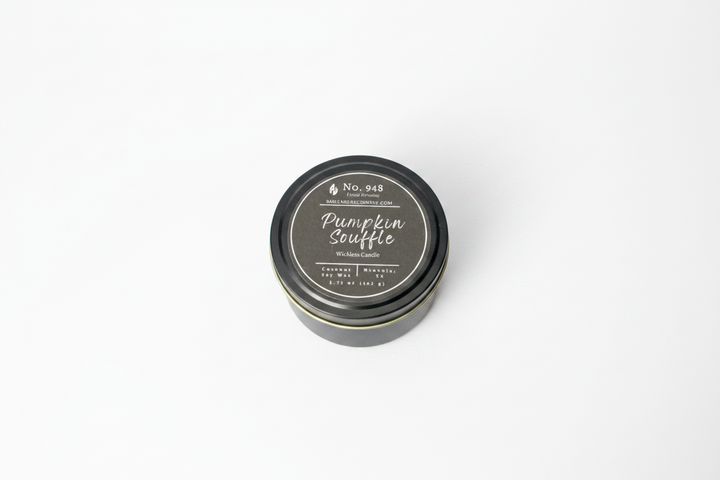 A small, round black tin labeled "Wickless Candle 5.75 oz" in coconut soy wax with "Pumpkin Souffle" and product details on the lid; available in 5.75 oz size.