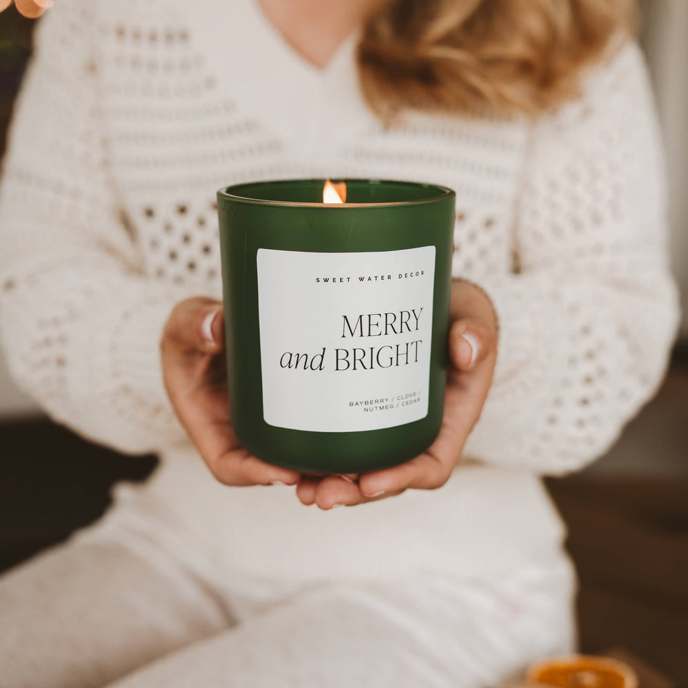 Merry and Bright 15 oz soy candle in a dark green jar with a white “MERRY and BRIGHT” label and a lit wick.