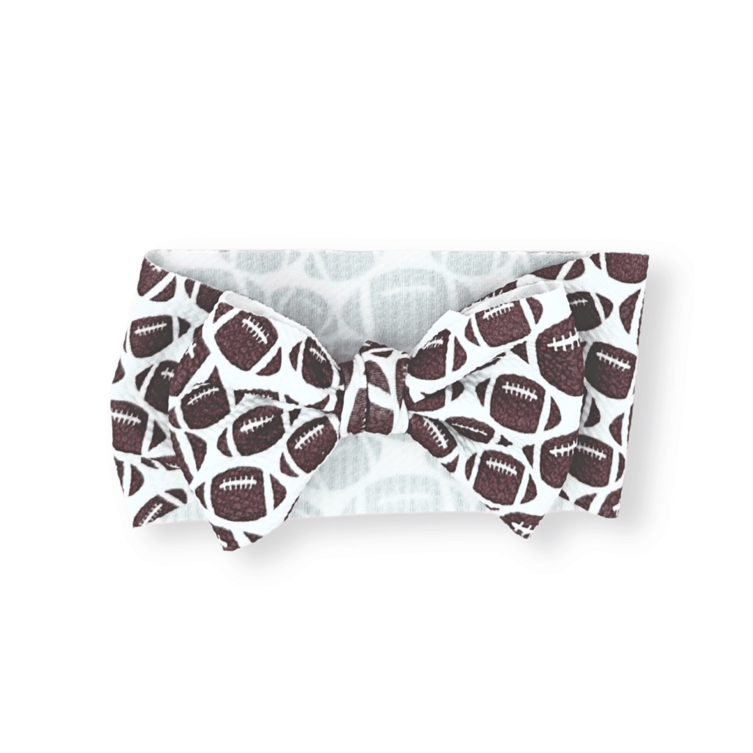 White bow tie head wrap with brown football pattern; available in newborn, infant, and toddler sizes.
