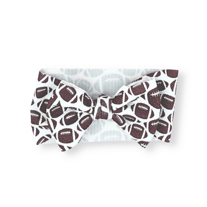 White bow tie head wrap with brown football pattern; available in newborn, infant, and toddler sizes.