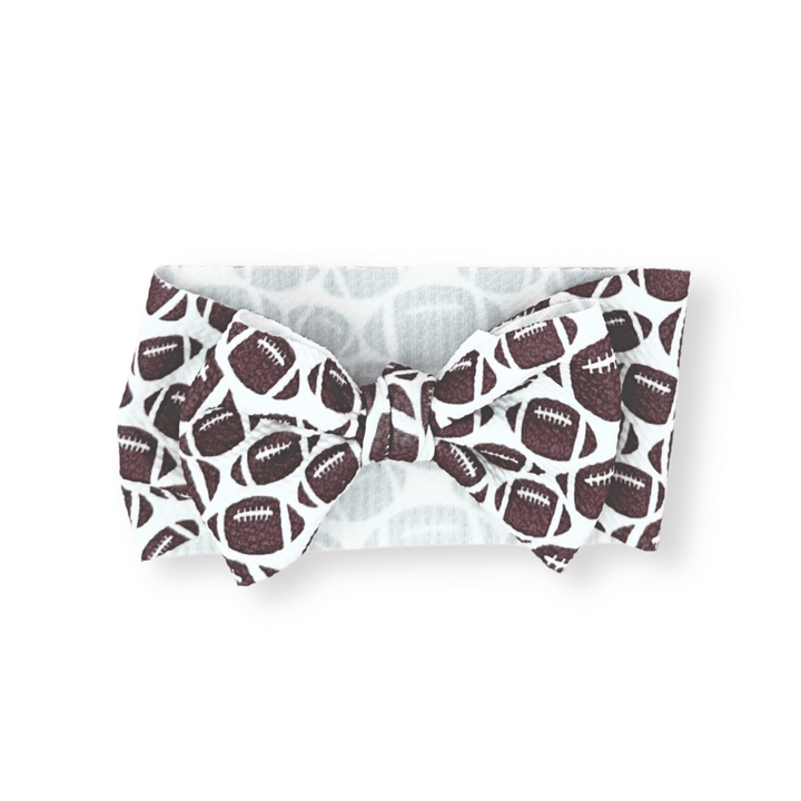 White bow tie head wrap with brown football pattern; available in newborn, infant, and toddler sizes.