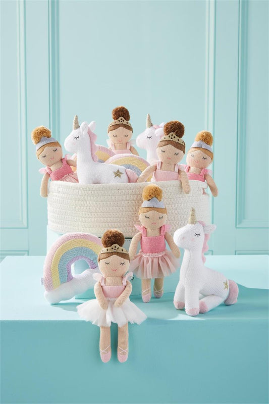 A collection of Rainbow Looms and plush toys, including unicorns and ballerina dolls, displayed on a white woven basket against a teal background.