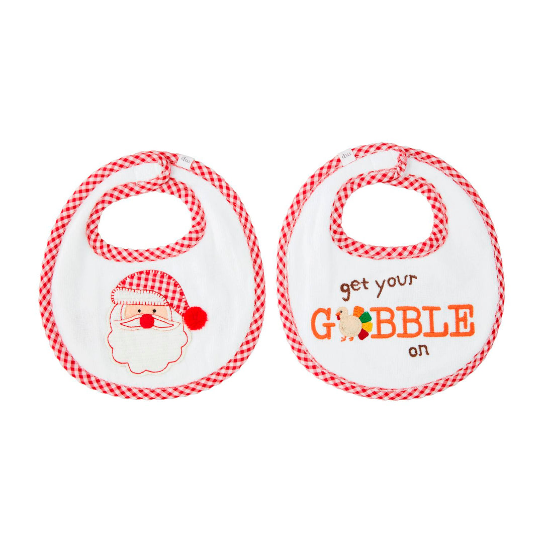 Boy Holiday Reversible Bibs: two white velour terry cloth bibs with red gingham binding, one with an embroidered Santa face and the other with “get your GOBBLE on” text and a turkey.