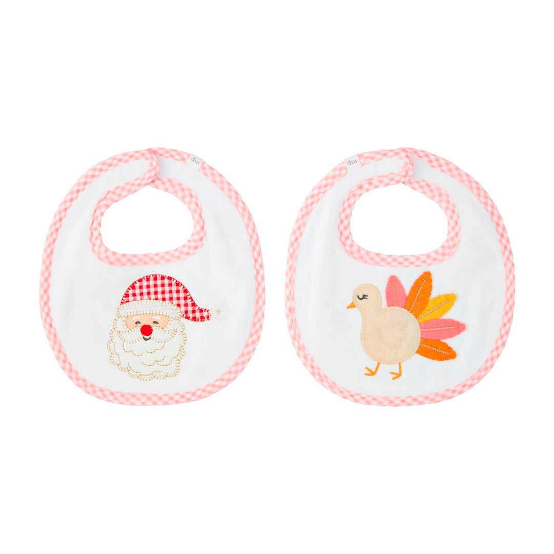 Girl Reversible Holiday Bibs: two white velour terry cloth baby bibs with pink gingham binding, featuring embroidered Santa Claus and turkey designs.