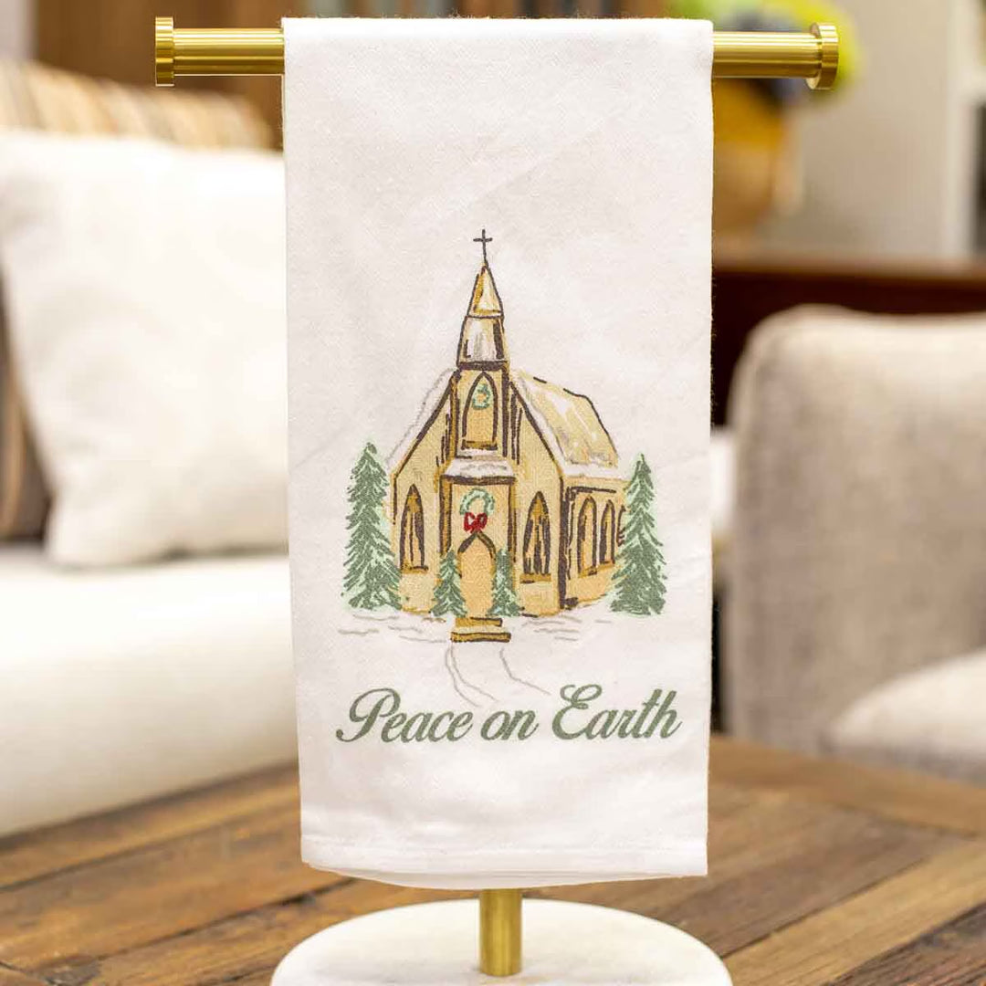 Peace on Earth hand towel, white fabric embroidered with a church, pine trees, and “Peace on Earth.”.
