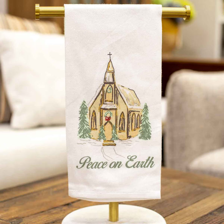 Peace on Earth hand towel, white fabric embroidered with a church, pine trees, and “Peace on Earth.”.