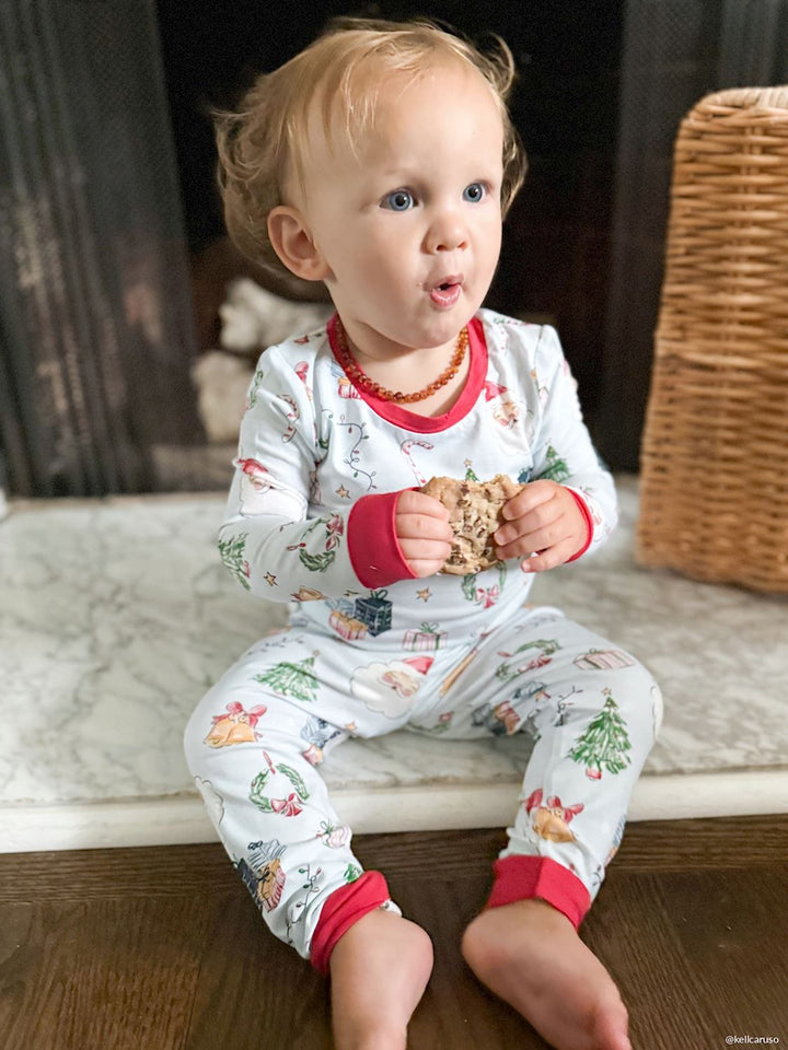 Blue Christmas Baby Sleeper: long-sleeved bamboo sleeper with a white background featuring a pattern of Christmas trees, gifts, and Santa Claus, finished with red trim. Available in all sizes.