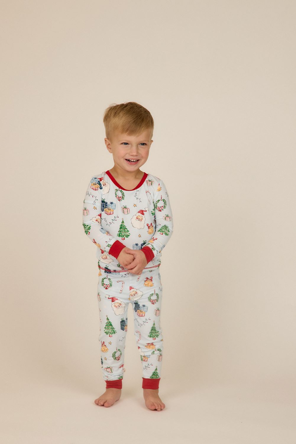 Light blue bamboo Little Kids Christmas pajamas with Santa, gift, tree, and wreath print, finished with red neck and cuff trim.