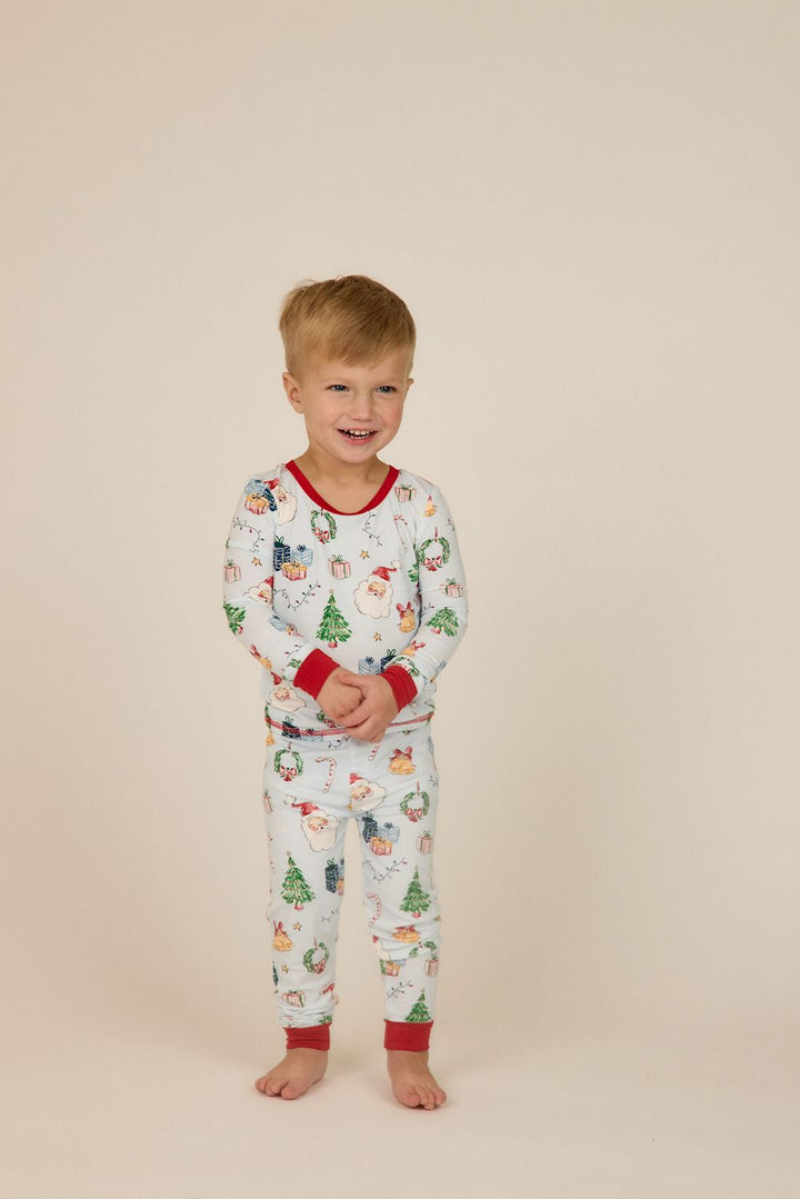 Light blue bamboo Little Kids Christmas pajamas with Santa, gift, tree, and wreath print, finished with red neck and cuff trim.