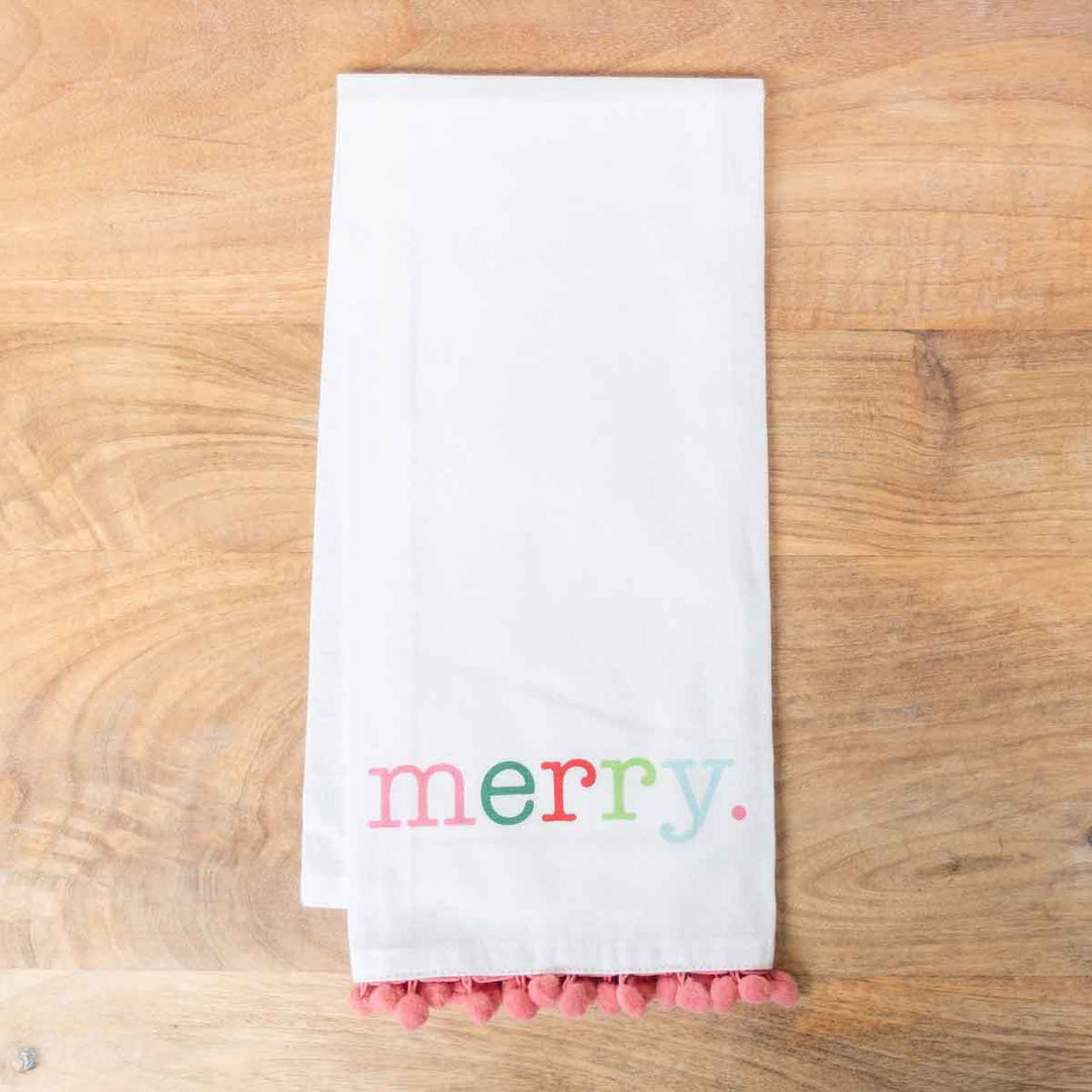 White Christmas hand towel featuring multicolored “merry” text and pink pom-pom trim.