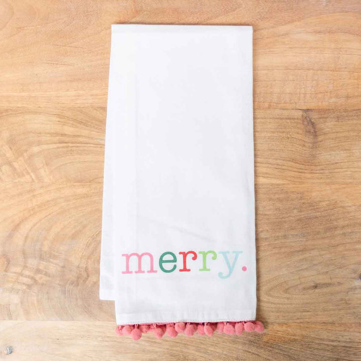 White Christmas hand towel featuring multicolored “merry” text and pink pom-pom trim.