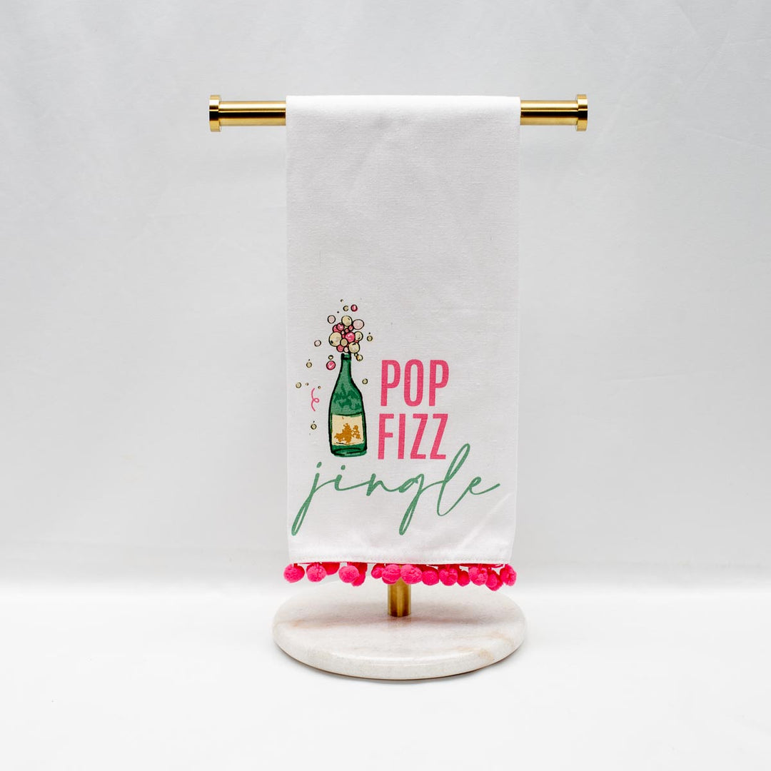 White Christmas hand towel with pink pom-pom trim, champagne bottle illustration, and “POP FIZZ jingle” text.