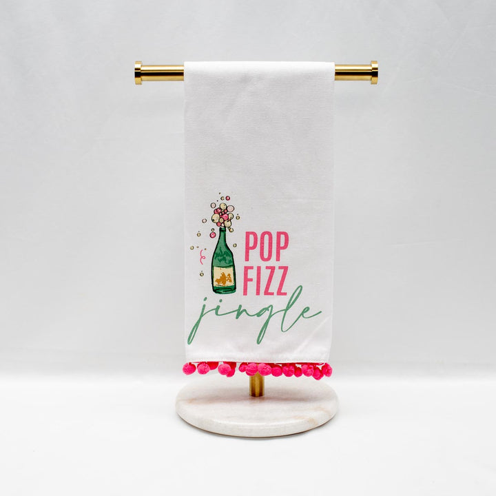 White Christmas hand towel with pink pom-pom trim, champagne bottle illustration, and “POP FIZZ jingle” text.