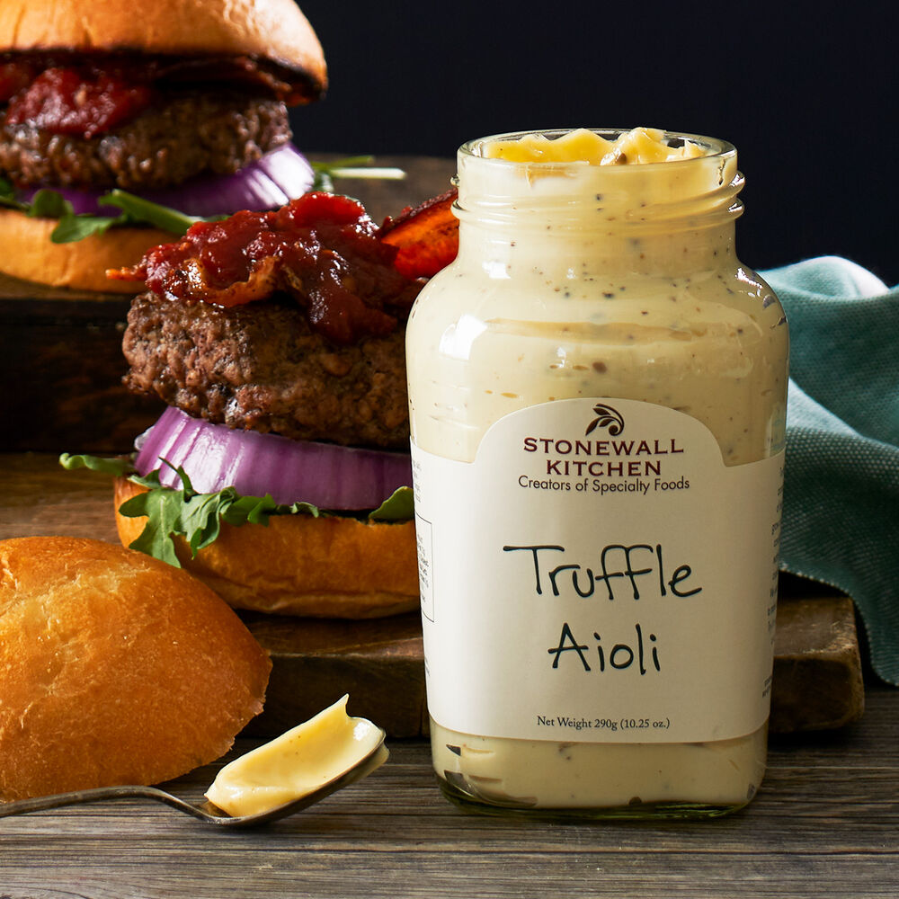 Truffle Aioli jar, 10.25 oz size, on wooden surface with a spoonful of aioli beside it.