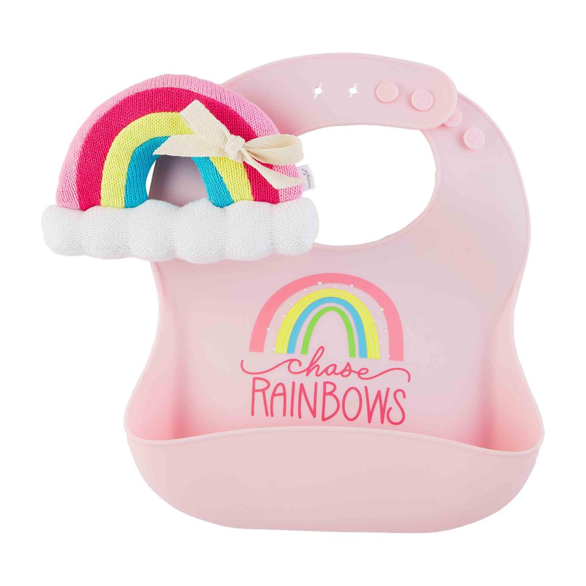 A Pink Rainbow Bib & Rattle Set featuring a colorful rainbow design and the phrase "chase rainbows" on the front. The bib has an adjustable neck closure and a plush cloud-and-rainbow handle at