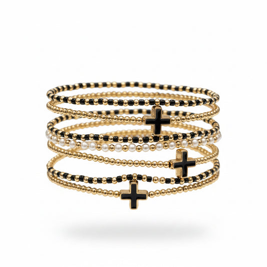 Seven gold beaded stretch bracelets with black, gold, and white beads, each featuring a bold black cross charm. Available in multiple sizes.