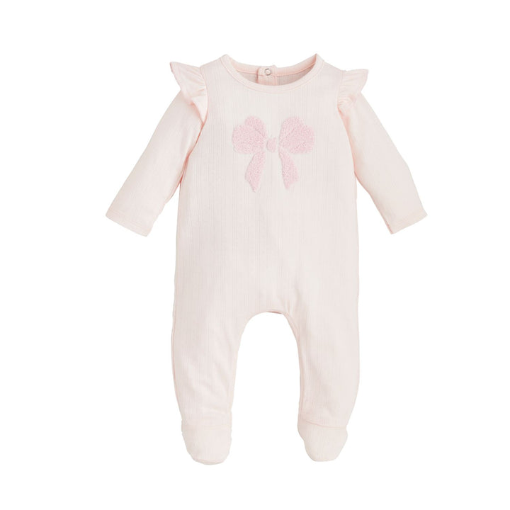 The Ruffle Bow Baby Sleeper is a light pink, soft cotton rib onesie with long sleeves and footed bottoms. It features a textured bow on the front and ruffle details on the shoulders. Available sizes: newborn, 0-3 months, 3-6 months.