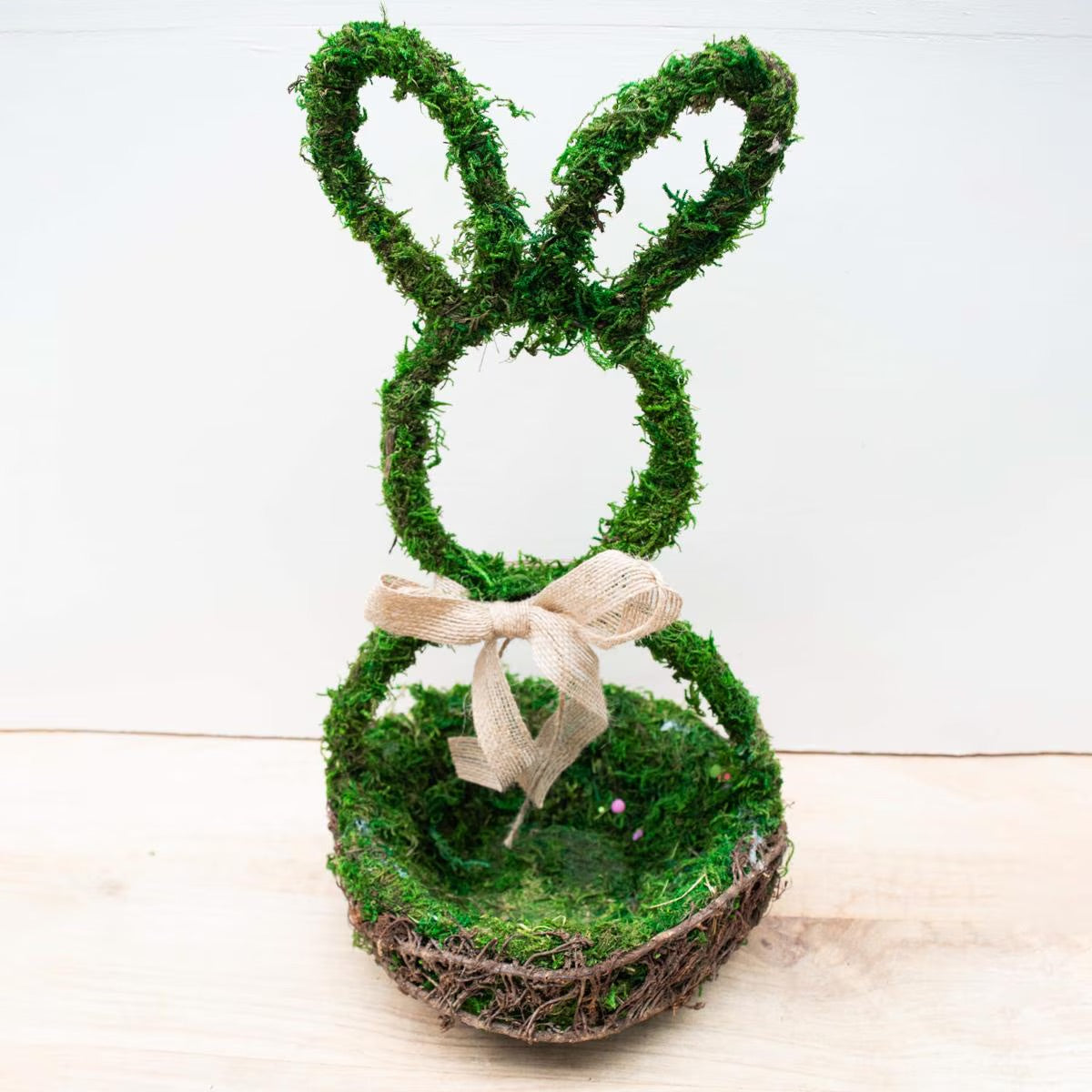 The Moss Bunny Basket is a bunny-shaped centerpiece made from twigs and moss, with a burlap ribbon. Available Sizes: One Size.