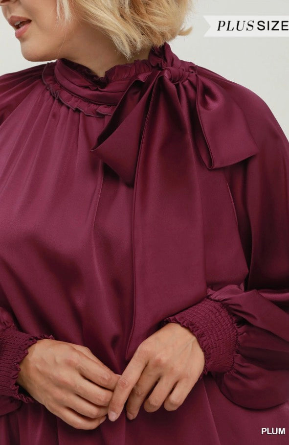 Shiny plum satin tie neck dress with long sleeves, bow at the neck, and smocked cuffs. Available in plus sizes.