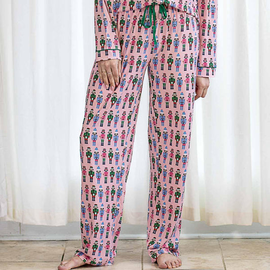 Festive holiday sleepwear featuring a nutcracker pattern. Includes pink Nutcracker March Sleep Pants and a long-sleeve shirt with green buttons and drawstring. Available sizes: S, M, L, XL.