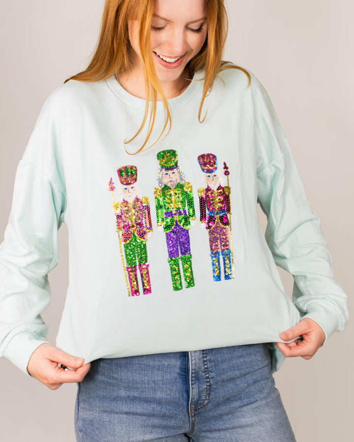 Light blue long-sleeve Candy Nutcracker Sequin Sweatshirt with three sequined nutcrackers. Available in various sizes.