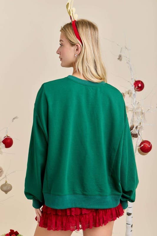 “Merry With Ornament Patchwork Oversized Long Sleeve Top” in hunter green. Available in sizes S–XL.