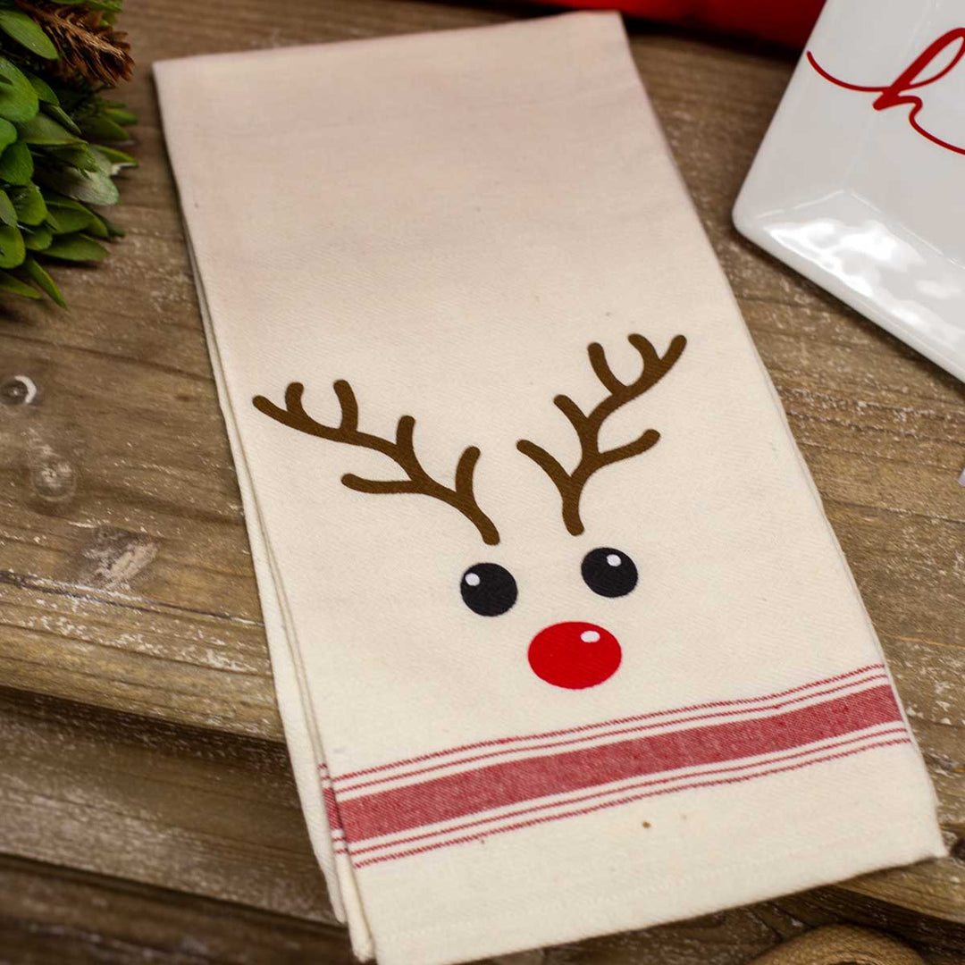Off-white Christmas hand towel with a reindeer face, red nose, brown antlers, and a red striped hem.