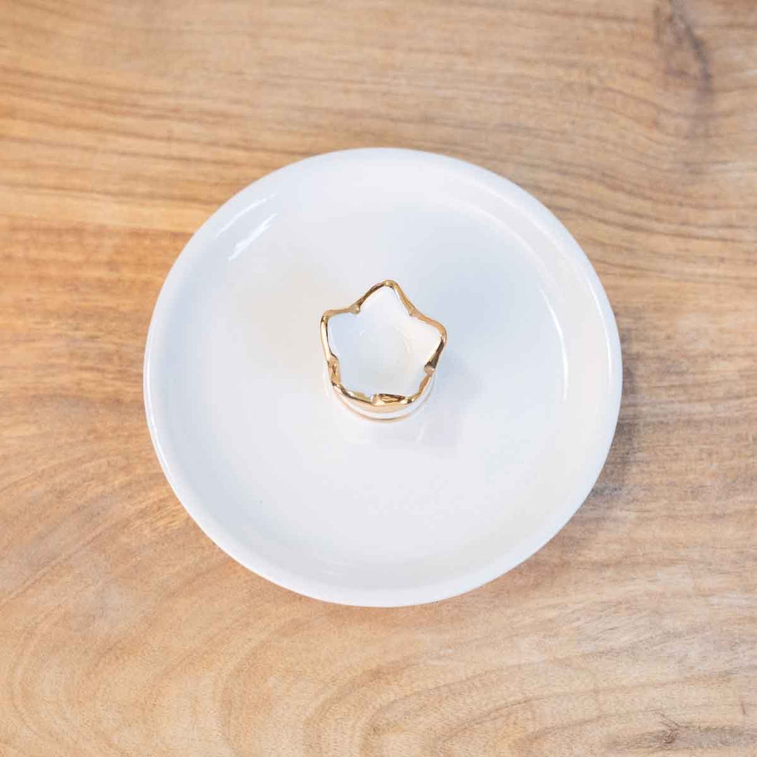 The Her Highness Trinket Dish is a star-shaped candle with a gold rim, set on a round white plate. Available in one size: 4"x4" dish.
