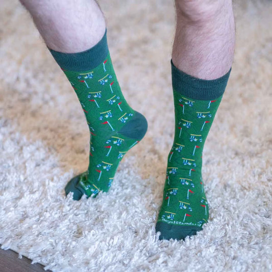 Men's Above Par Socks feature playful golf course patterns with red flags and holes, made from combed cotton. Available in sizes M and L.
