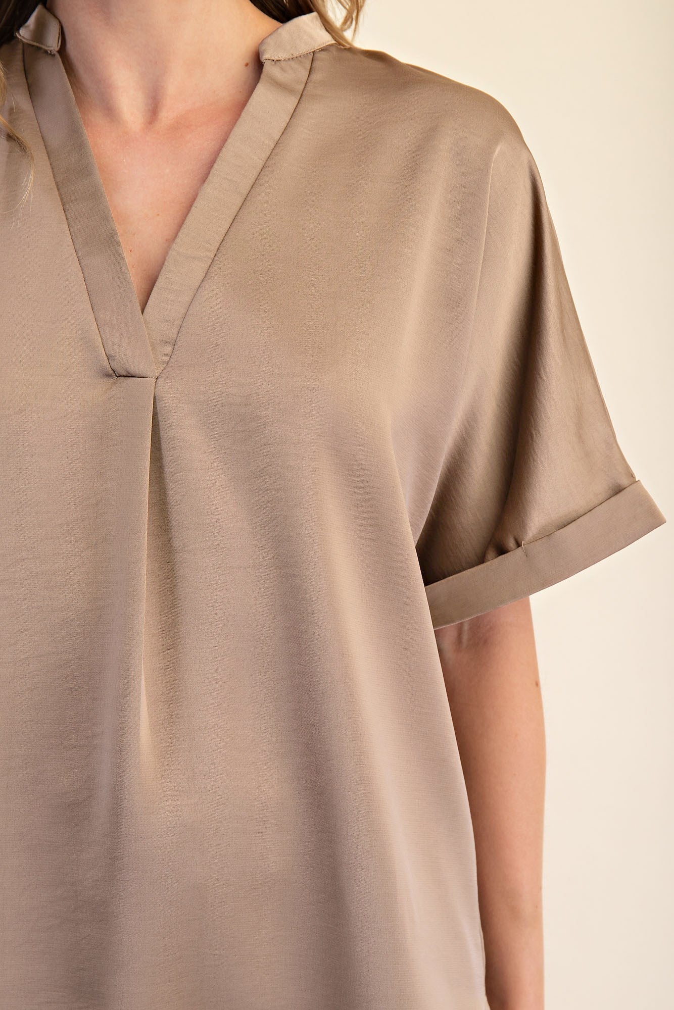 Tan V-neck placket top with cuffed short sleeves and subtle sheen. Lightweight fabric. Available in sizes XS–XL.