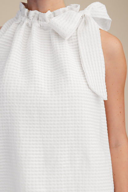 White Ruffle Neck Tie Sleeveless Top with ruffled neckline, large shoulder bow, subtle checkered pattern. Sizes XS-XL available.