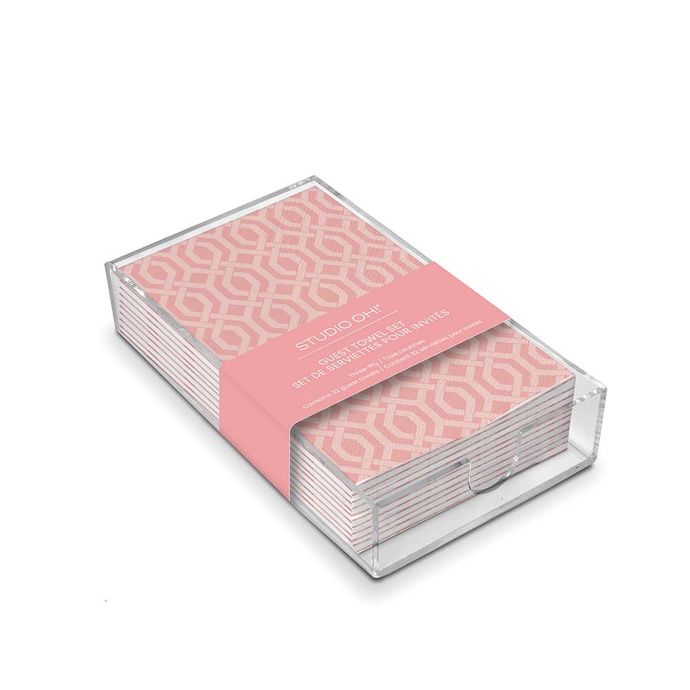 Pink 3-ply guest towels with a white geometric design in a clear acrylic holder, labeled "STUDIO OH!". Sizes not listed.