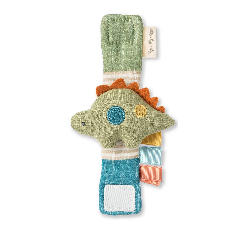 A colorful, textured Itzy Bitzy Wrist Rattle: Cottage dinosaur plush toy in a vertical position with stitched details and various fabric patterns. The toy has a green body, blue, yellow, and orange spots, and a gentle facial expression.