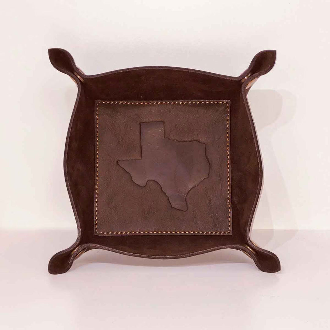The Leather Embossed Valet Tray is a dark brown, square-based catchall with curved edges and a stitched Texas outline at the center. Ideal for nightstands or as a gift for him. Available in one size.