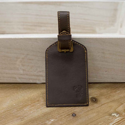 The Leather Embossed Luggage Tag features brown leather with yellow stitching, a strap, and a buckle. Sizes available: One-size fits all.