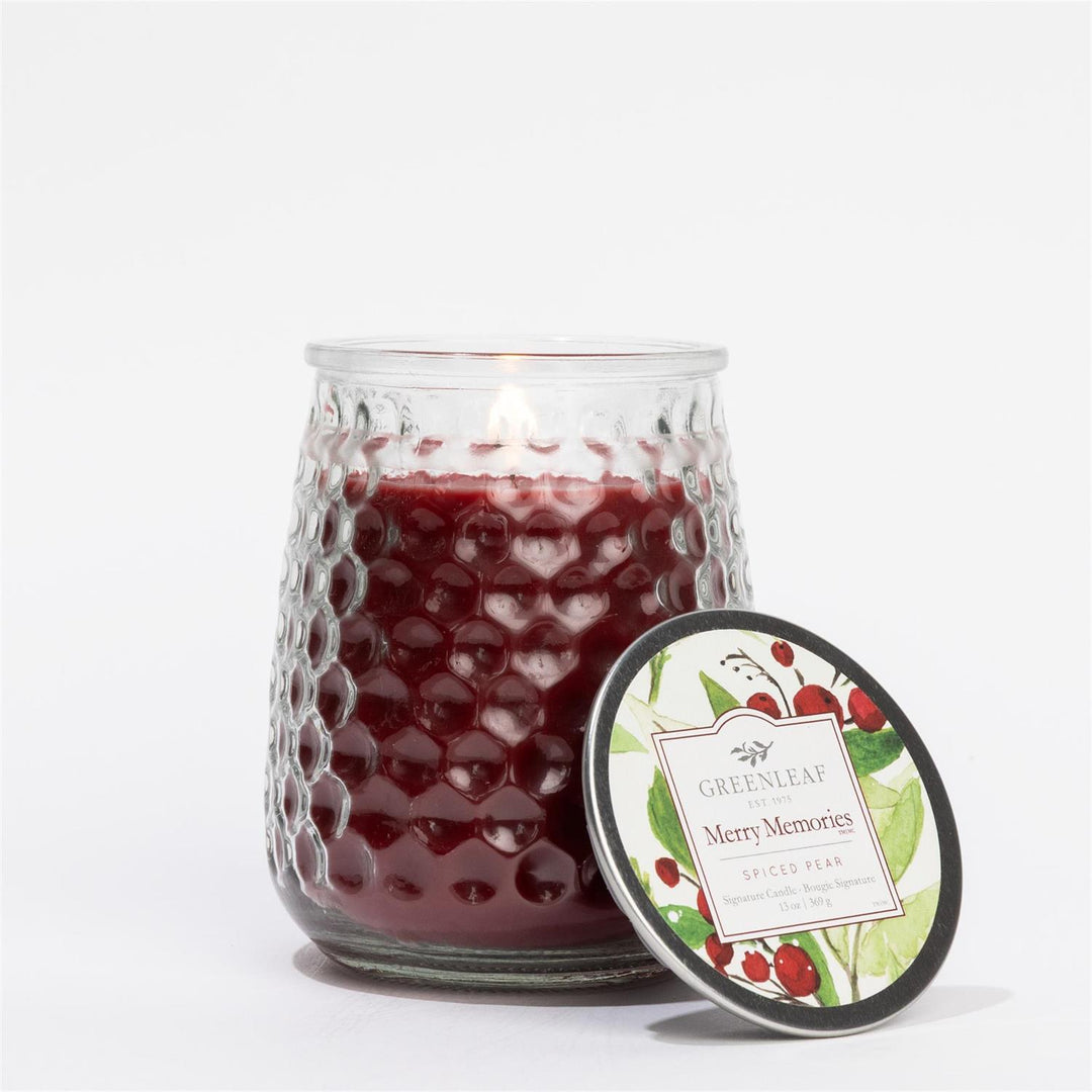 Lit dark red Merry Memories Signature Candle in a textured glass jar with a botanical lid, 13 oz / 369 g.