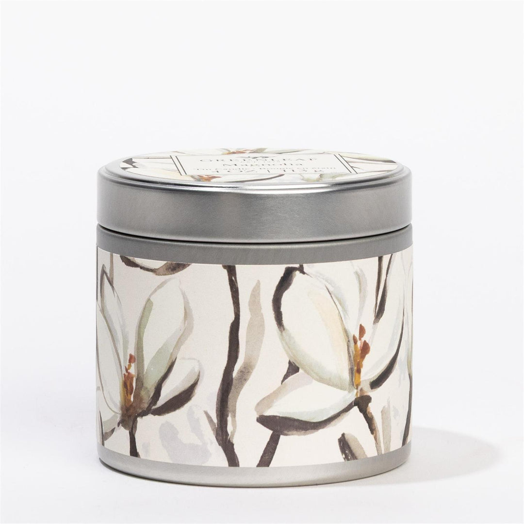 Magnolia Tin Candle: round metal tin with lid, white magnolia design, magnolia scent; sizes: 4oz, 8oz.