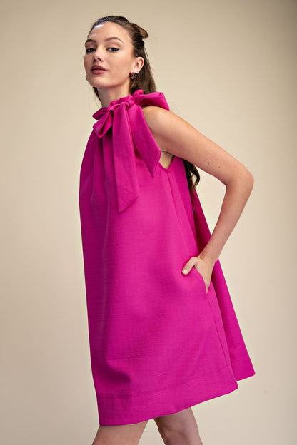 Magenta Tie-Neck Sleeveless Dress with one-shoulder bow and pockets. Available in sizes XS-XL.