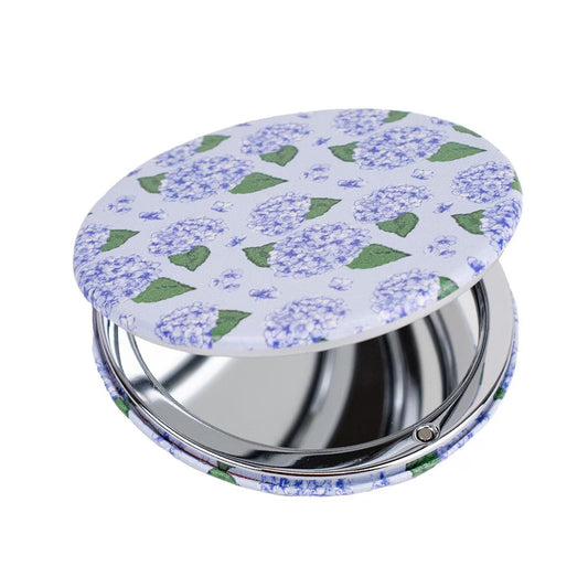 A pocket mirror featuring a floral design with purple hydrangeas and green leaves. Compact size for easy portability.