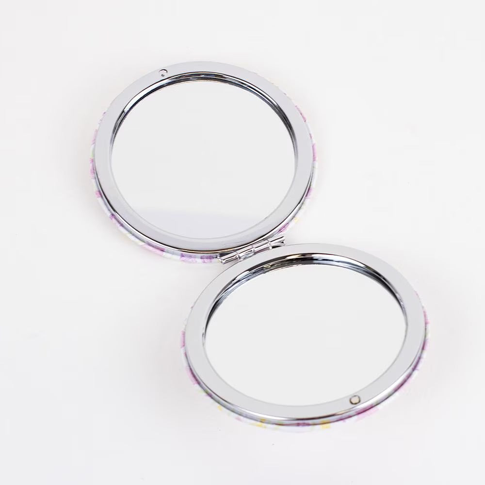 The Pocket Mirror is a round compact with pink and yellow speckles, featuring clean mirrors framed by a thin silver rim. Sizes available: N/A.