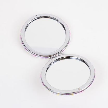 The Pocket Mirror is a round compact with pink and yellow speckles, featuring clean mirrors framed by a thin silver rim. Sizes available: N/A.