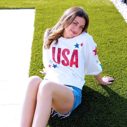Millie USA Top: white, bold red "USA," colorful stars. Available in XS-XL.