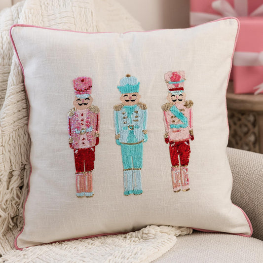 The Sequin Nutcrackers Square Pillow features three embroidered sequin nutcrackers in vibrant pink, blue, and red uniforms with unique hats. Available size: 18" x 18".