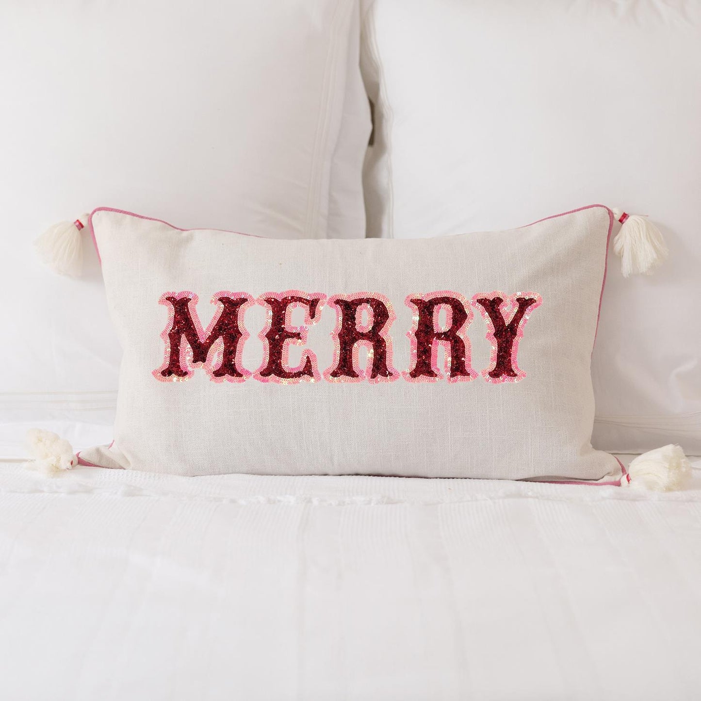 The Merry Lumbar Pillow adds holiday cheer with red sequin "MERRY" letters on white. It has corner tassels and thin red trim. Available in one size.